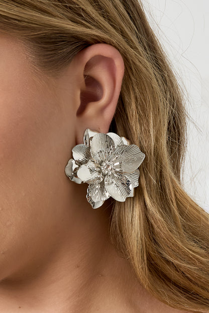 Close-up side view of model wearing silver flower statement earring with rhinestone center