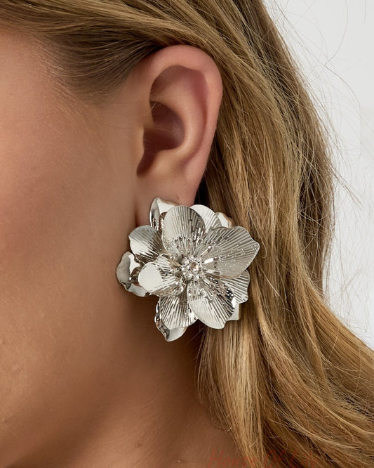 Close-up side view of model wearing silver flower statement earring with rhinestone center