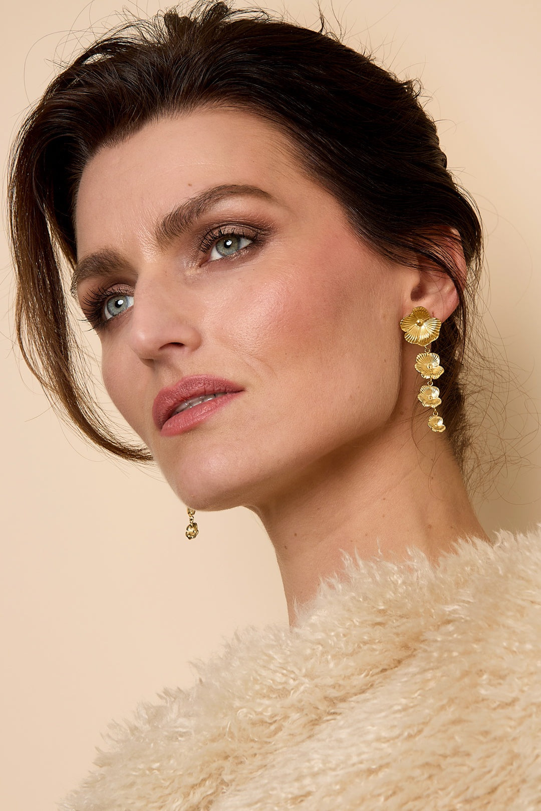 Model wearing gold floral cascade dangle earrings with soft makeup and beige fuzzy sweater