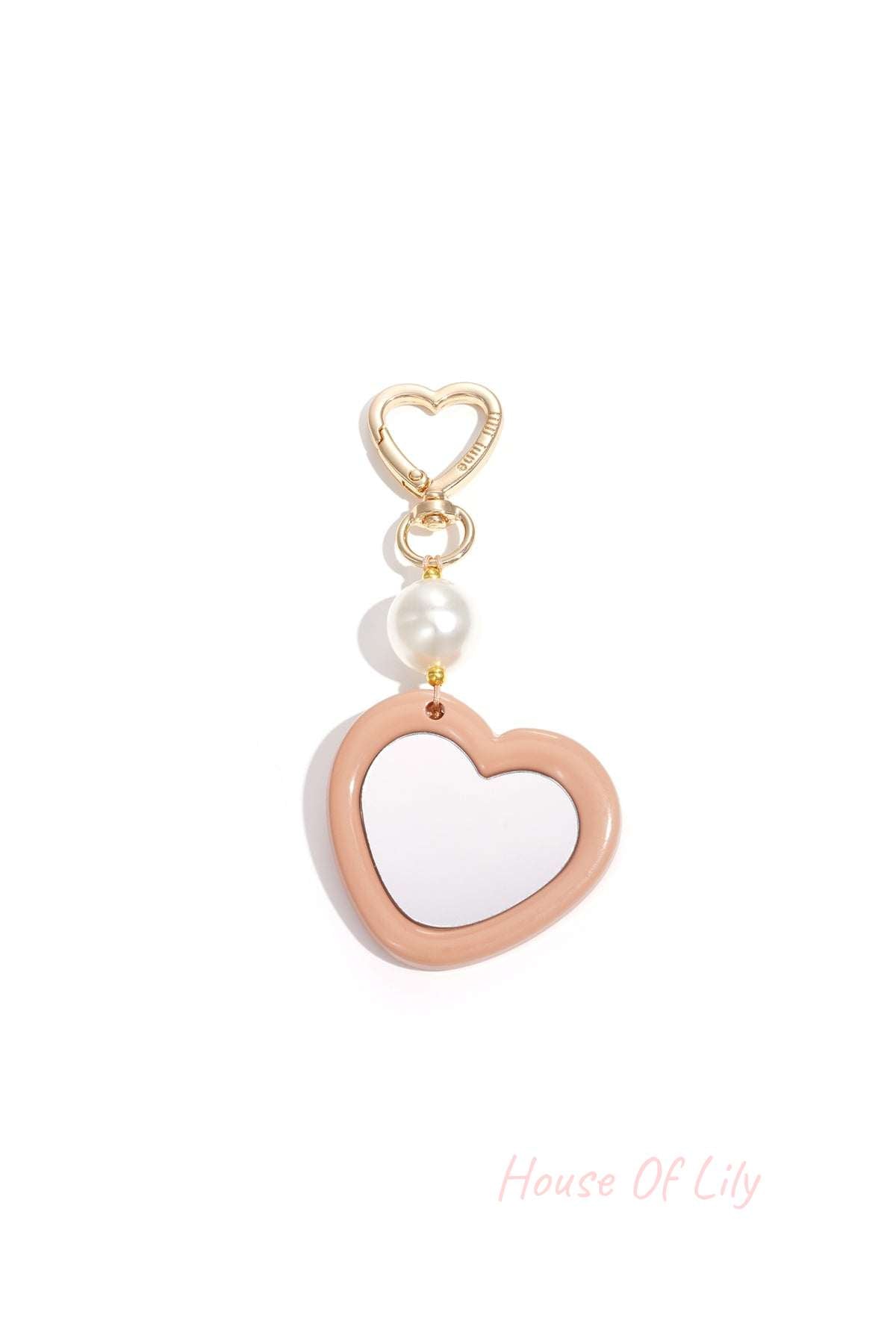 Gold heart clip holding gold-tone metal heart charm outlined with pearl bead on white background