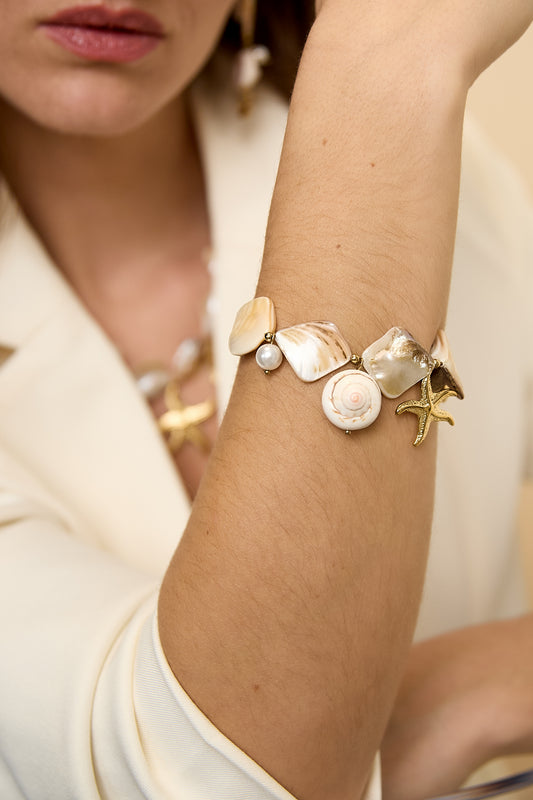 Mother Pearl Sea Charm bracelet featuring white shell segments, a round pearl, and a gold starfish charm on a wrist.