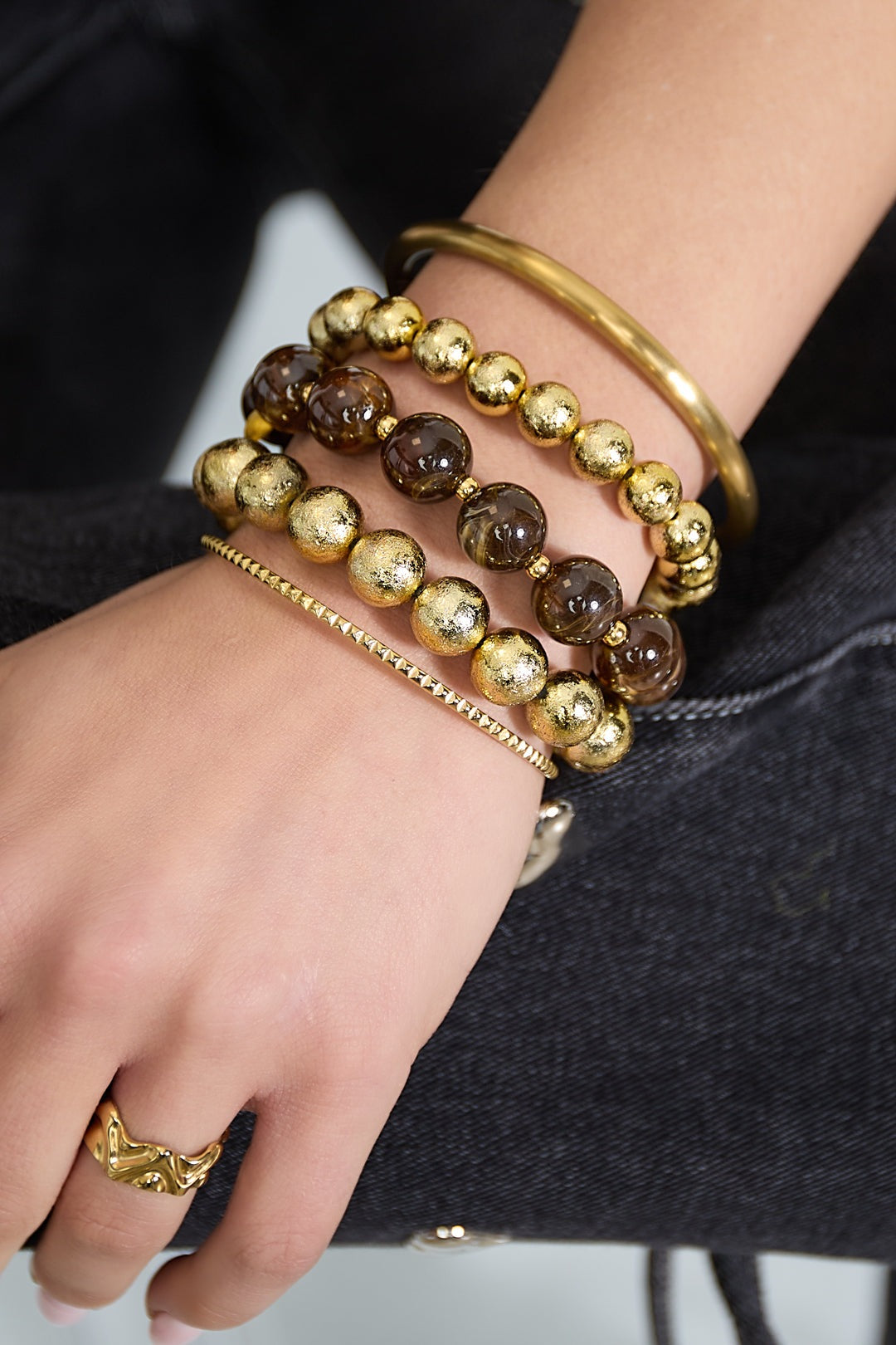 Close-up of wrist wearing multiple bracelets including brown marbled and textured gold bead bracelets with a gold bangle
