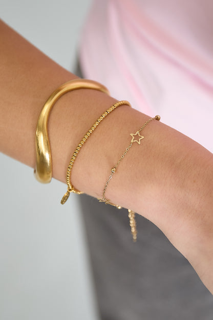 Close-up of a wrist wearing gold star chain bracelet stacked with other gold bracelets and pink top