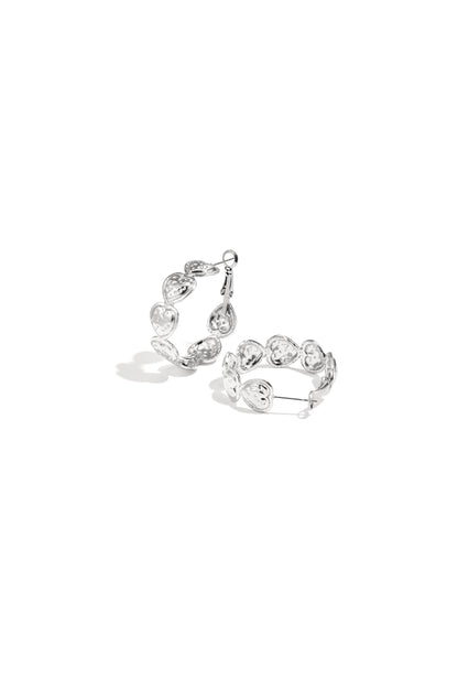 Pair of silver hoop earrings composed of small embossed hearts arranged in a circle on a white background