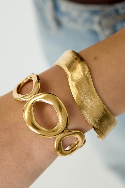 Close-up of a wrist wearing a gold curved minimalist cuff bracelet paired with an artistic gold open circle bracelet