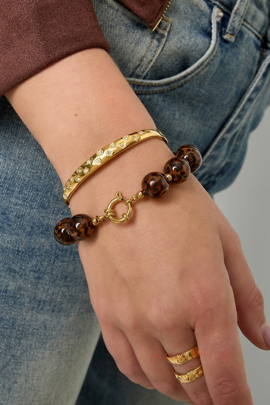 Model wearing gold-tone bangle with crystal accents and a tortoiseshell bead bracelet paired with gold rings, with denim and brown jacket