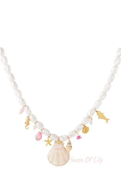 White faux pearl necklace with gold-tone seafood charms including scallop shell, starfish, seahorse, and pink fish accents on a plain white background