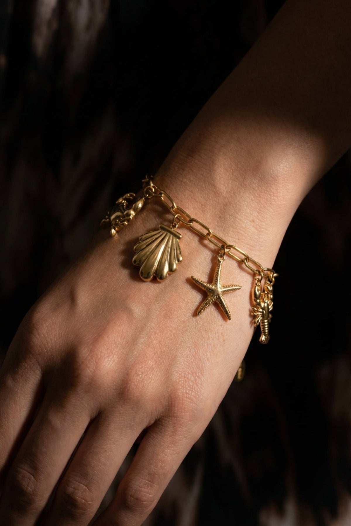 Gold bracelet with shell and starfish charms on a wrist against a dark background