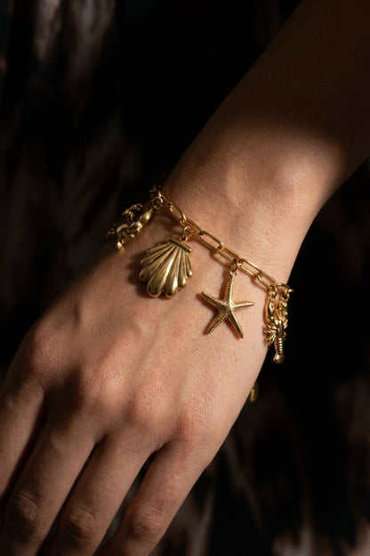 Gold bracelet with shell and starfish charms on a wrist against a dark background