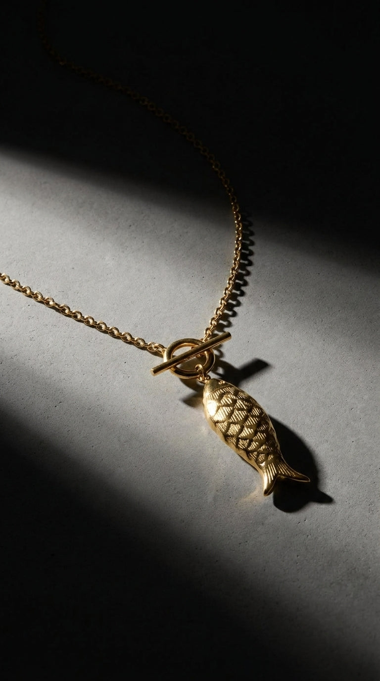 Gold Catching Vibes necklace featuring a textured fish pendant on a delicate chain with a front toggle clasp.