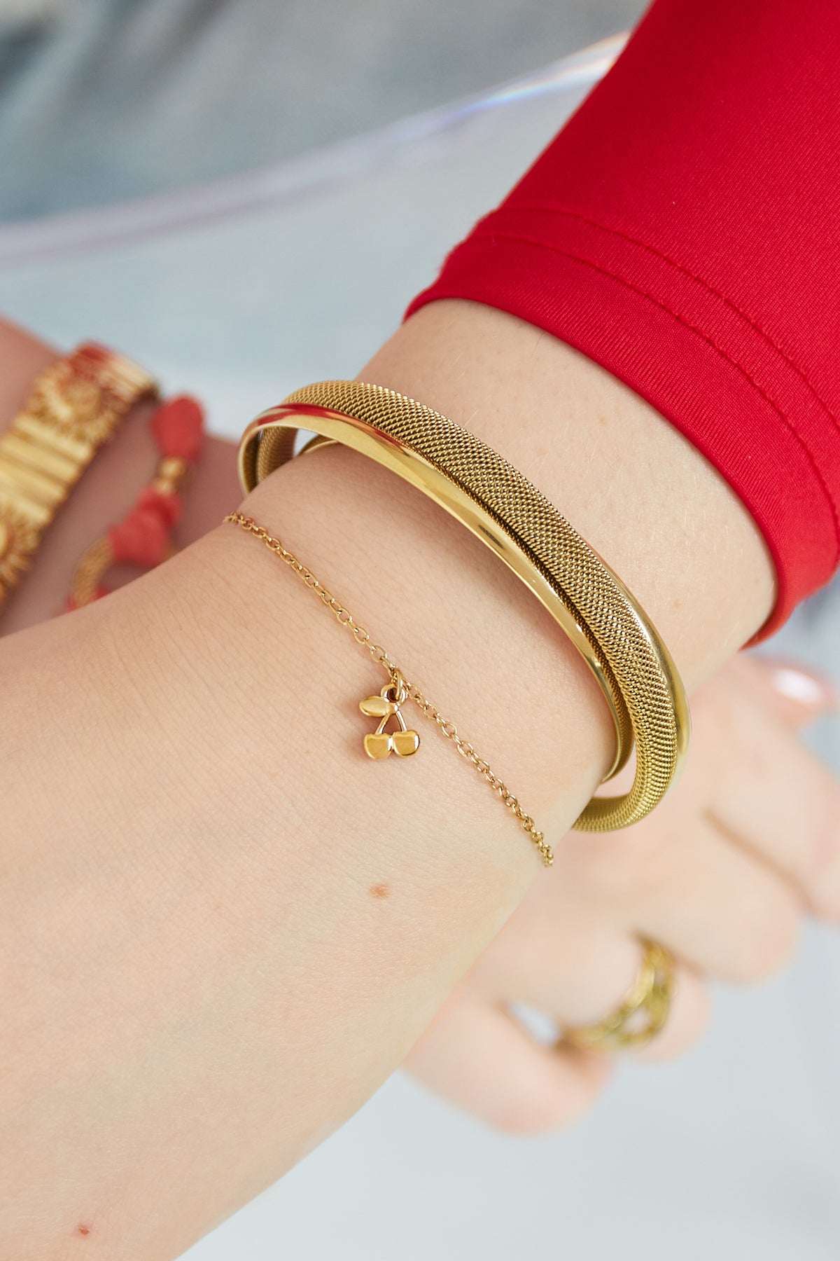 Model wearing the golden cherry charm bracelet alongside complementary gold bangles and a red sleeve