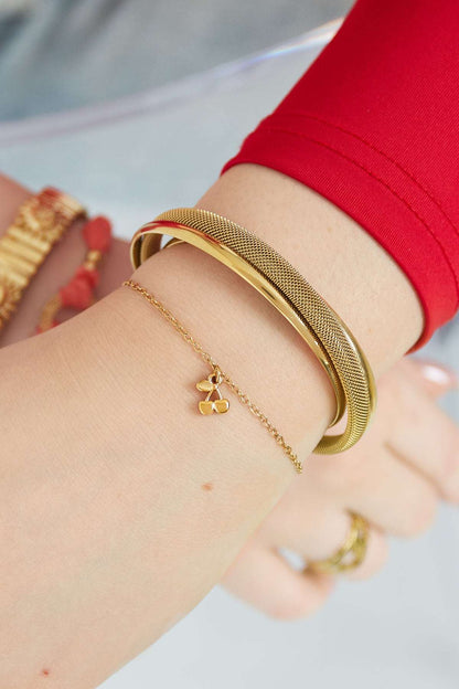 Model wearing the golden cherry charm bracelet alongside complementary gold bangles and a red sleeve