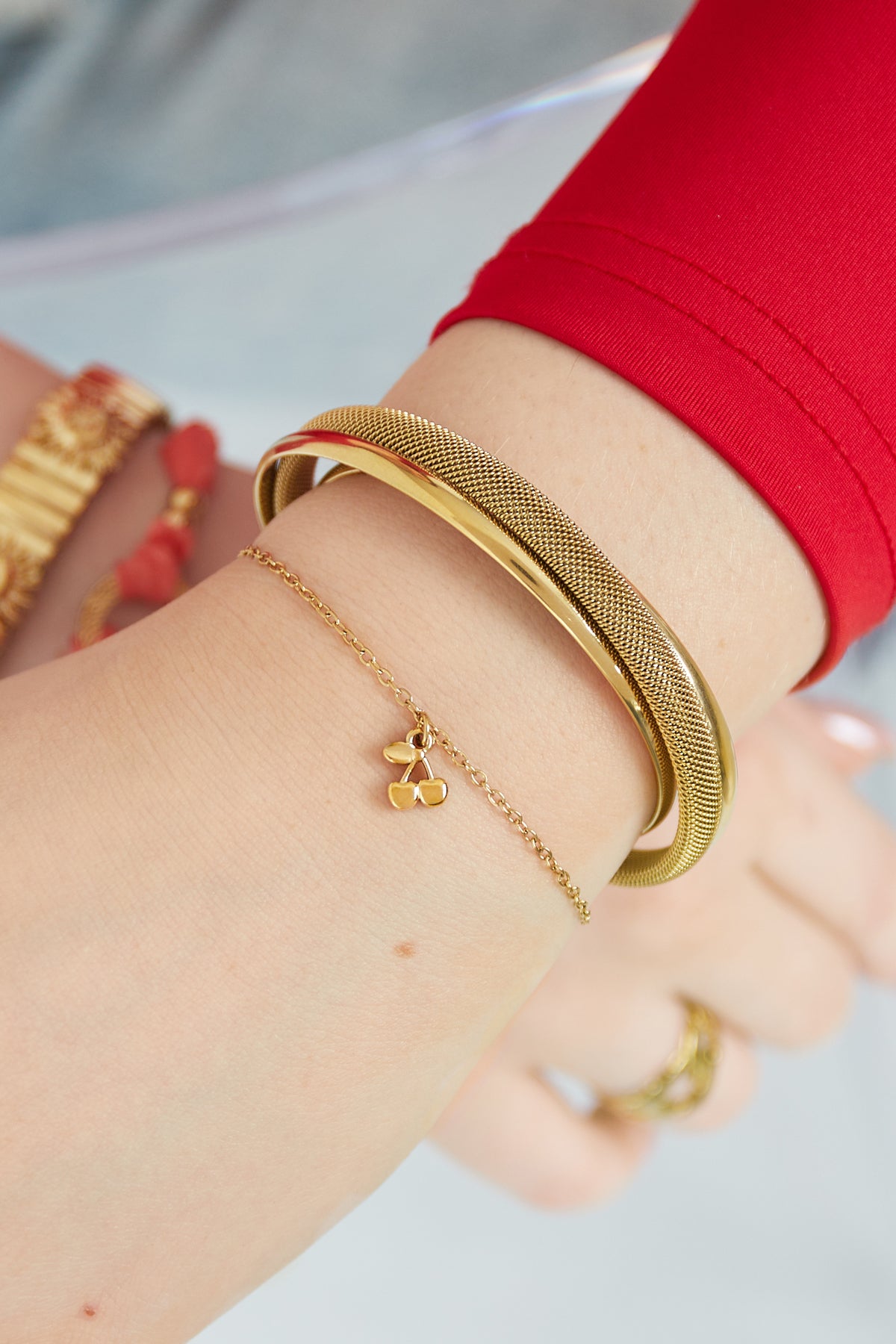 Model wearing the golden cherry charm bracelet alongside complementary gold bangles and a red sleeve
