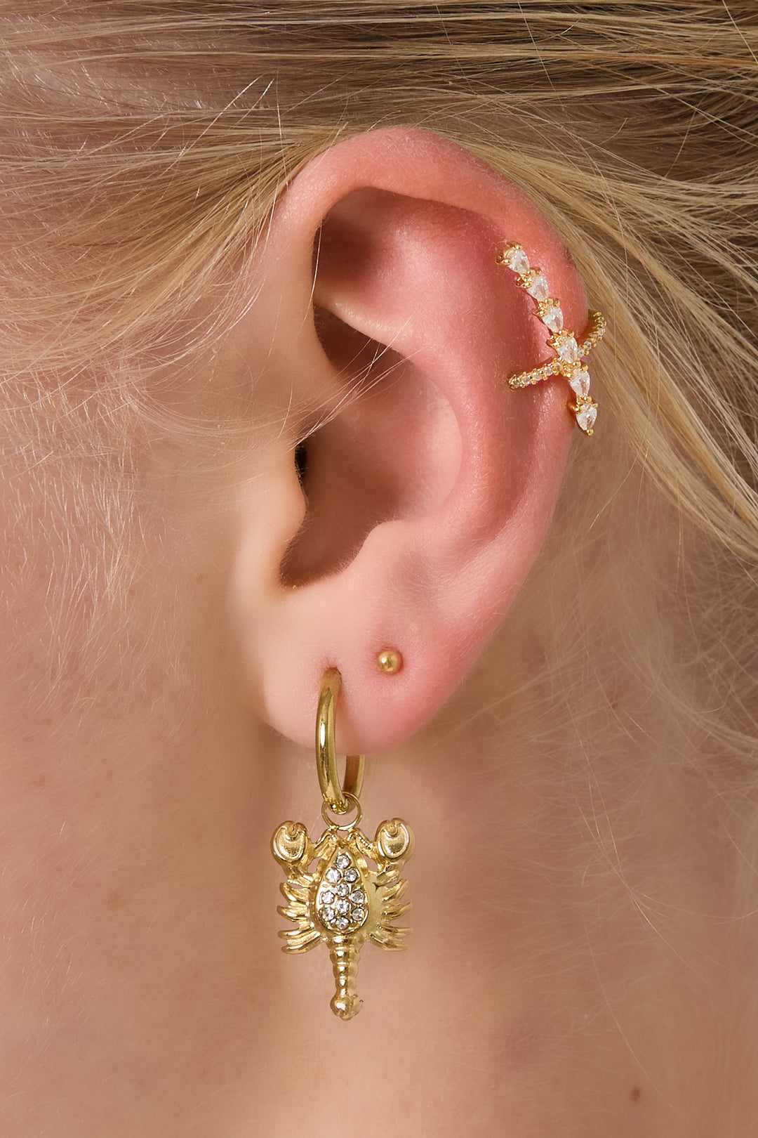 Close-up of ear adorned with gold ear cuff featuring pear-shaped cubic zirconia stones and gold scorpion charm hoop earring