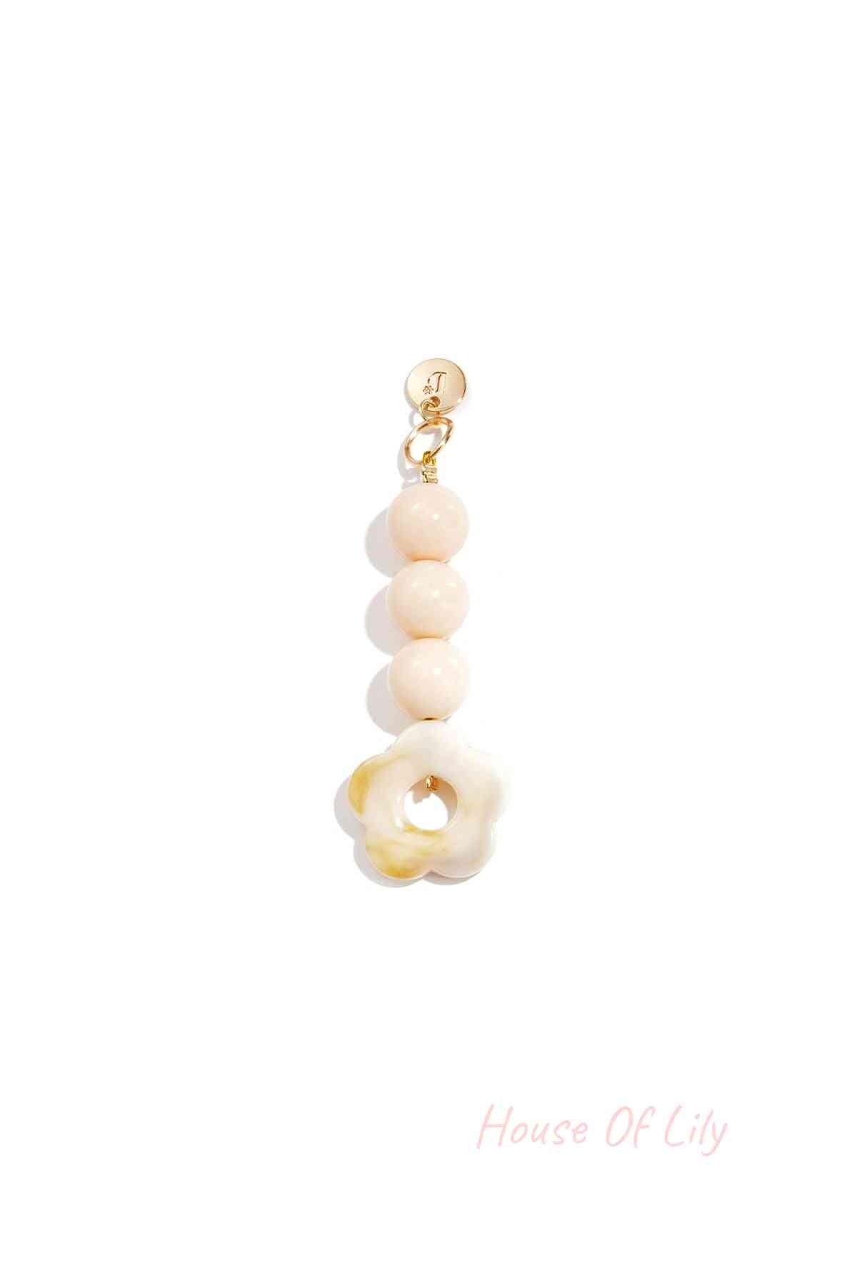Creamy white marbled acrylic flower bag charm with three round beige beads hanging from a gold clasp on white background