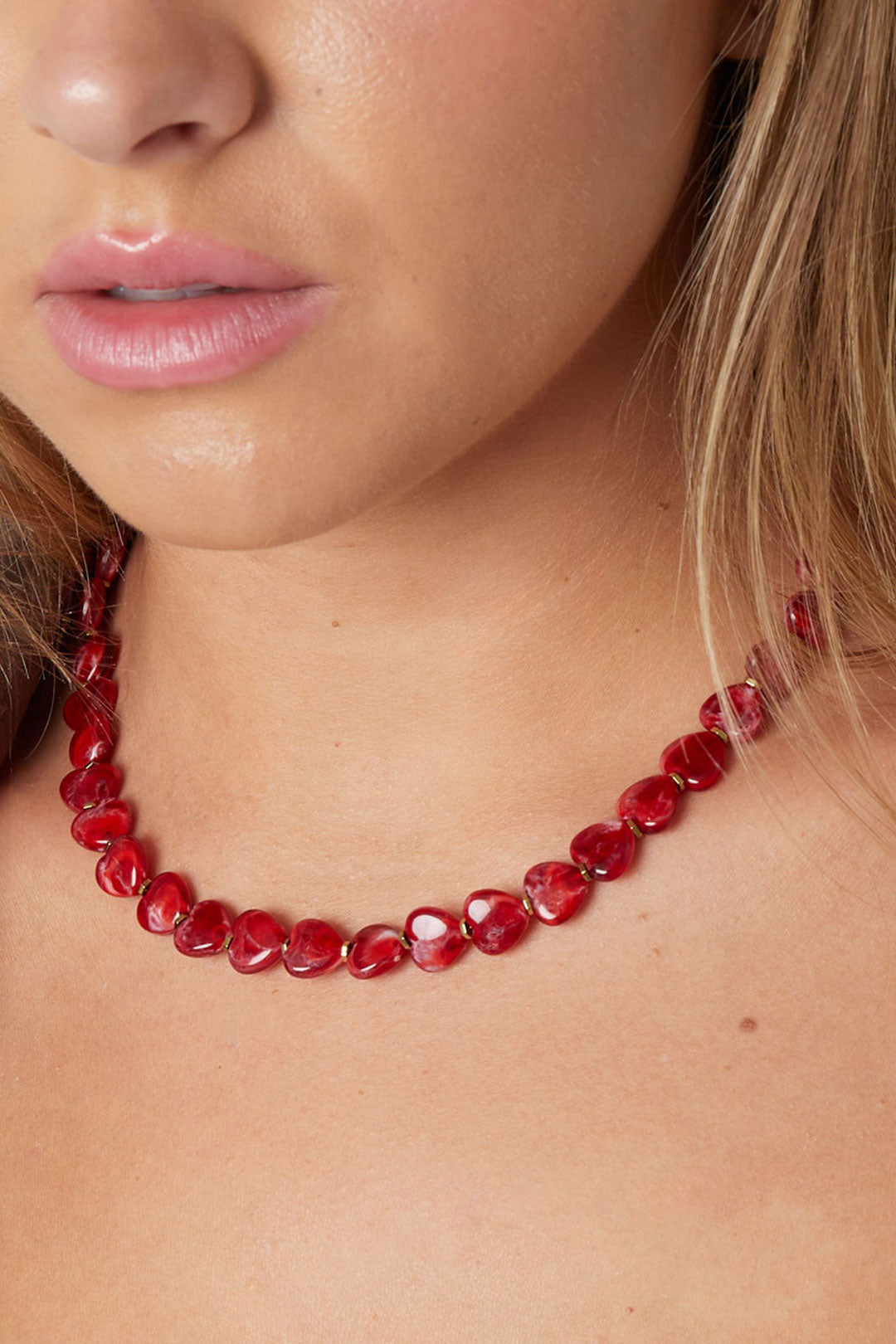 Close-up of the red heart-shaped acrylic bead necklace worn close to the neck highlighting glossy finish and marbled details