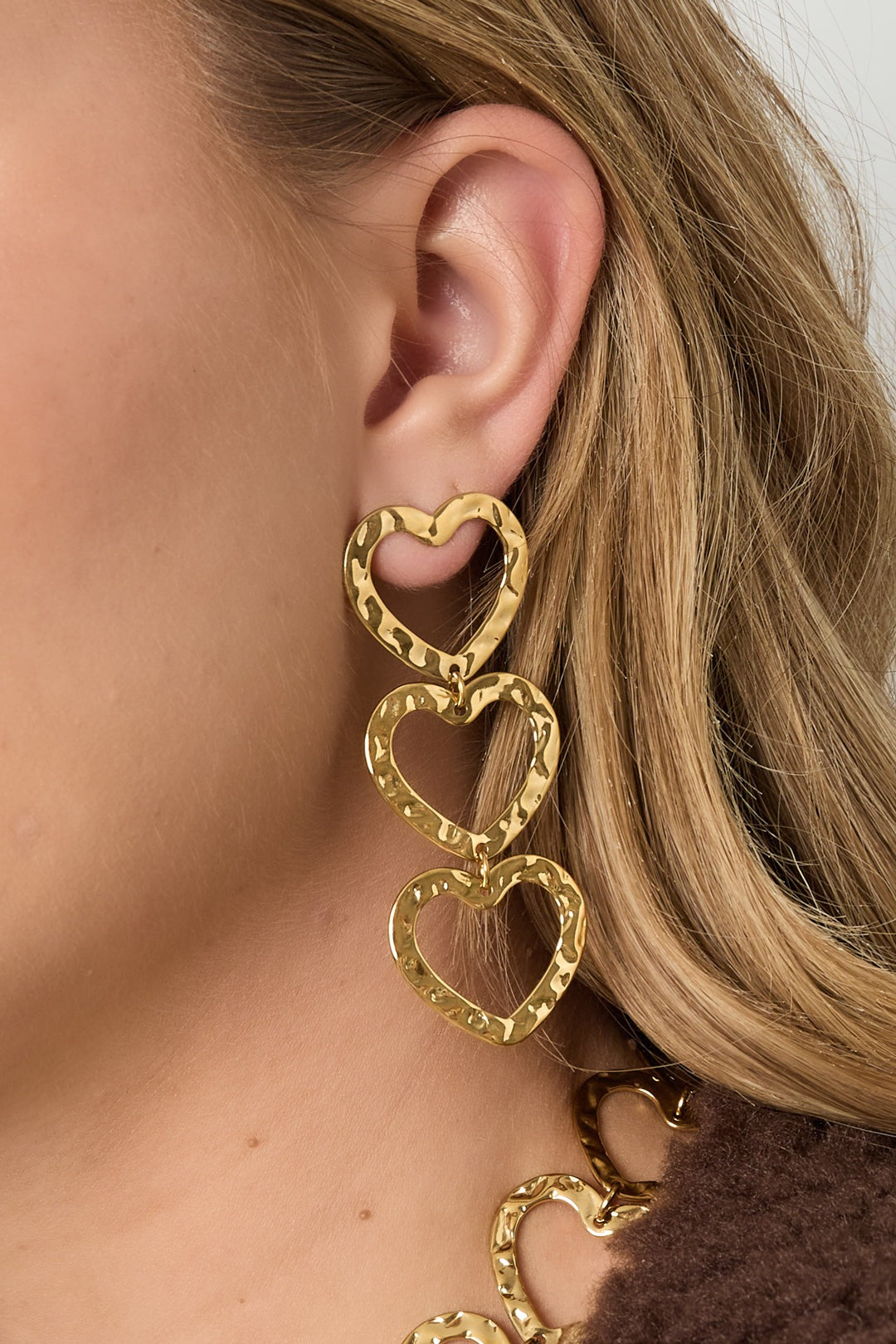 Close detail of woman's ear showcasing gold hammered triple heart dangle earrings