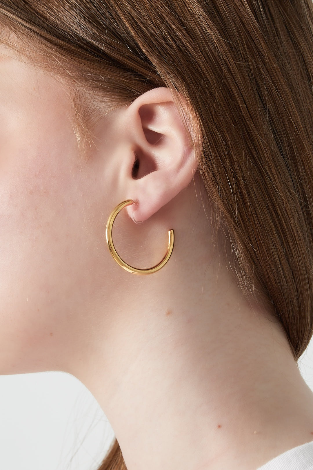 Close-up side profile of model wearing a gold clip-on hoop earring showing minimalist style
