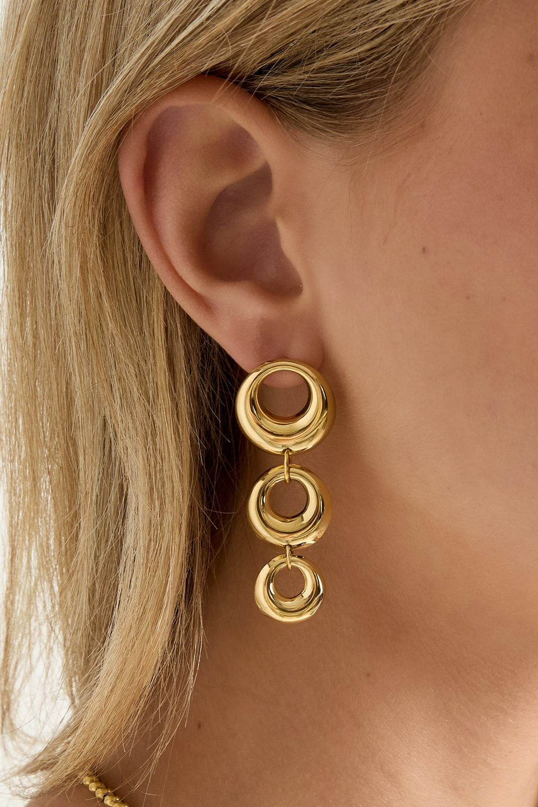 Close-up of woman wearing one chunky linked circle gold dangle earring highlighting polished finish