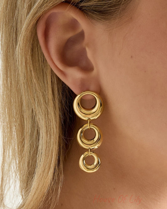 Close-up of woman wearing one chunky linked circle gold dangle earring highlighting polished finish