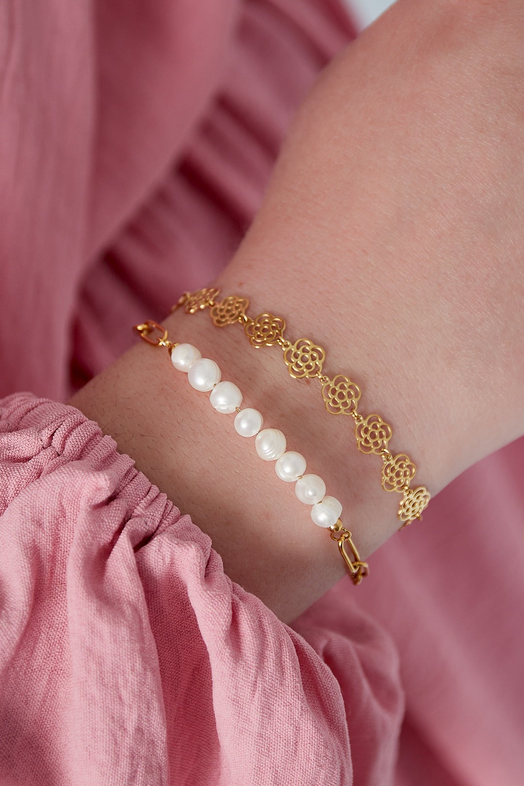 Close-up of wrist wearing gold tone rose link bracelet paired with a pearl bead bracelet, styled with pink fabric sleeve