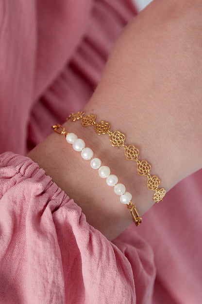 Close-up of wrist wearing gold tone rose link bracelet paired with a pearl bead bracelet, styled with pink fabric sleeve