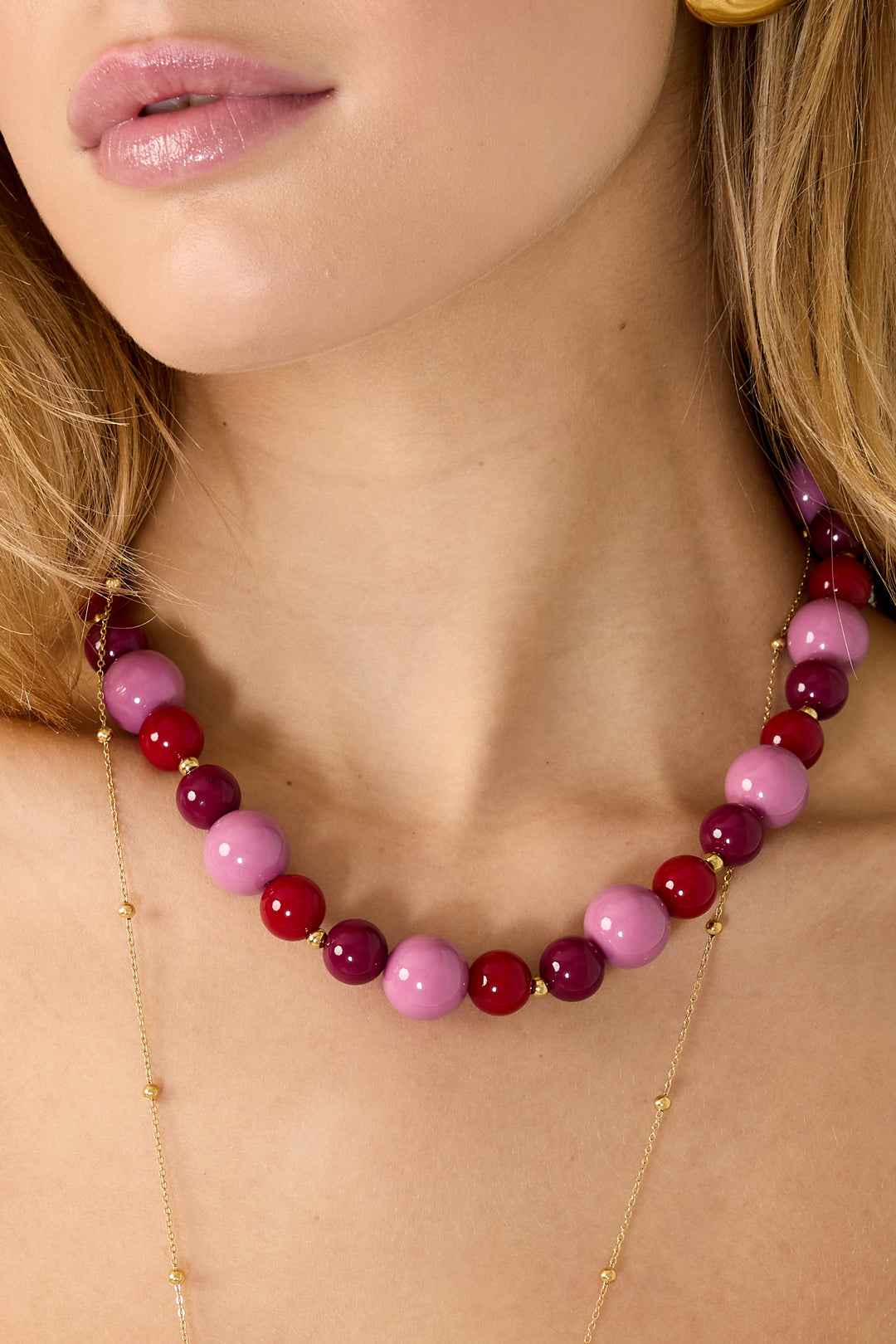 Close-up of model's neck showcasing pink and red glossy chunky beaded necklace with gold accent beads