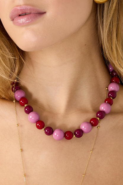 Close-up of model's neck showcasing pink and red glossy chunky beaded necklace with gold accent beads