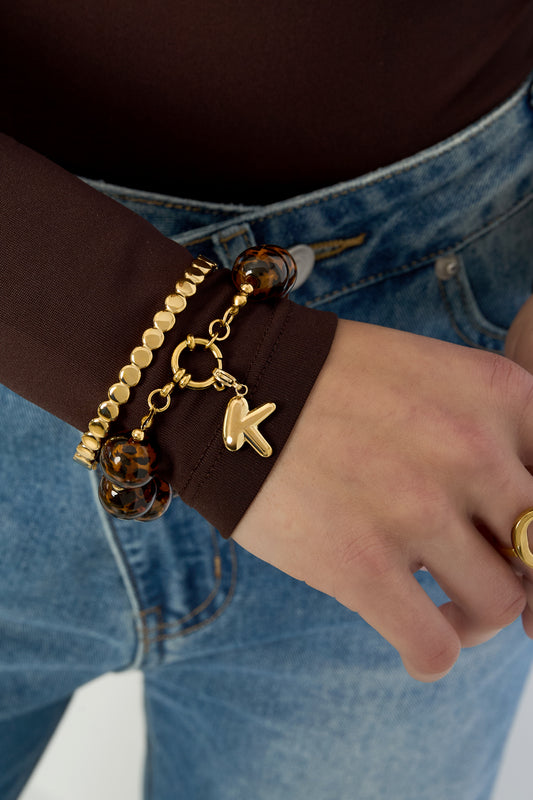 Bracelet worn on wrist paired with gold beads bracelet and gold ring, styled with brown top and denim jeans