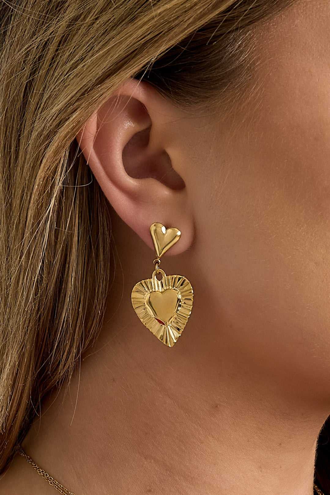 Gold-tone heart drop earrings featuring intricate embossed detailing displayed on white background