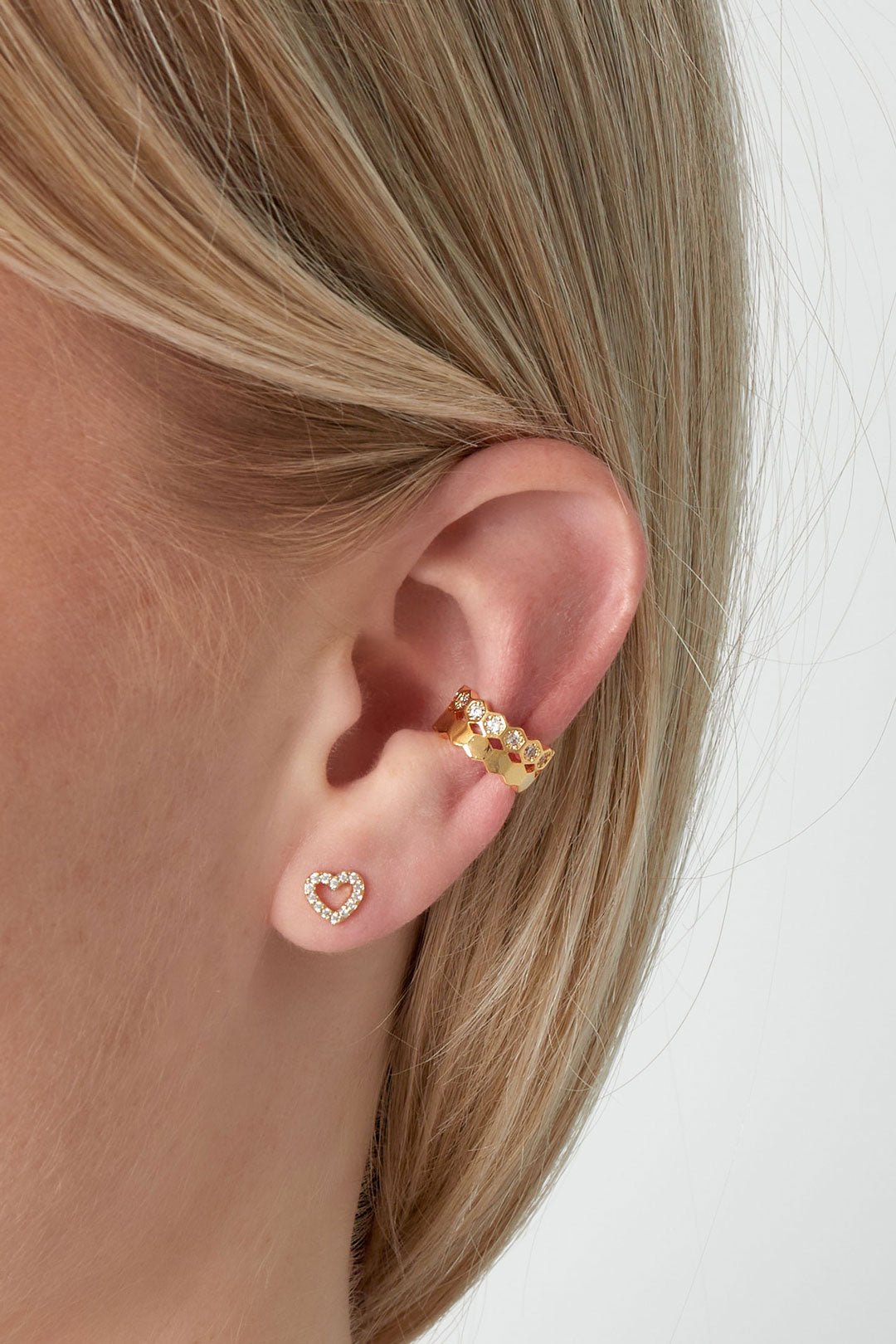 Side view of a woman wearing the gold geometric ear cuff on her ear with a heart-shaped stud earring below