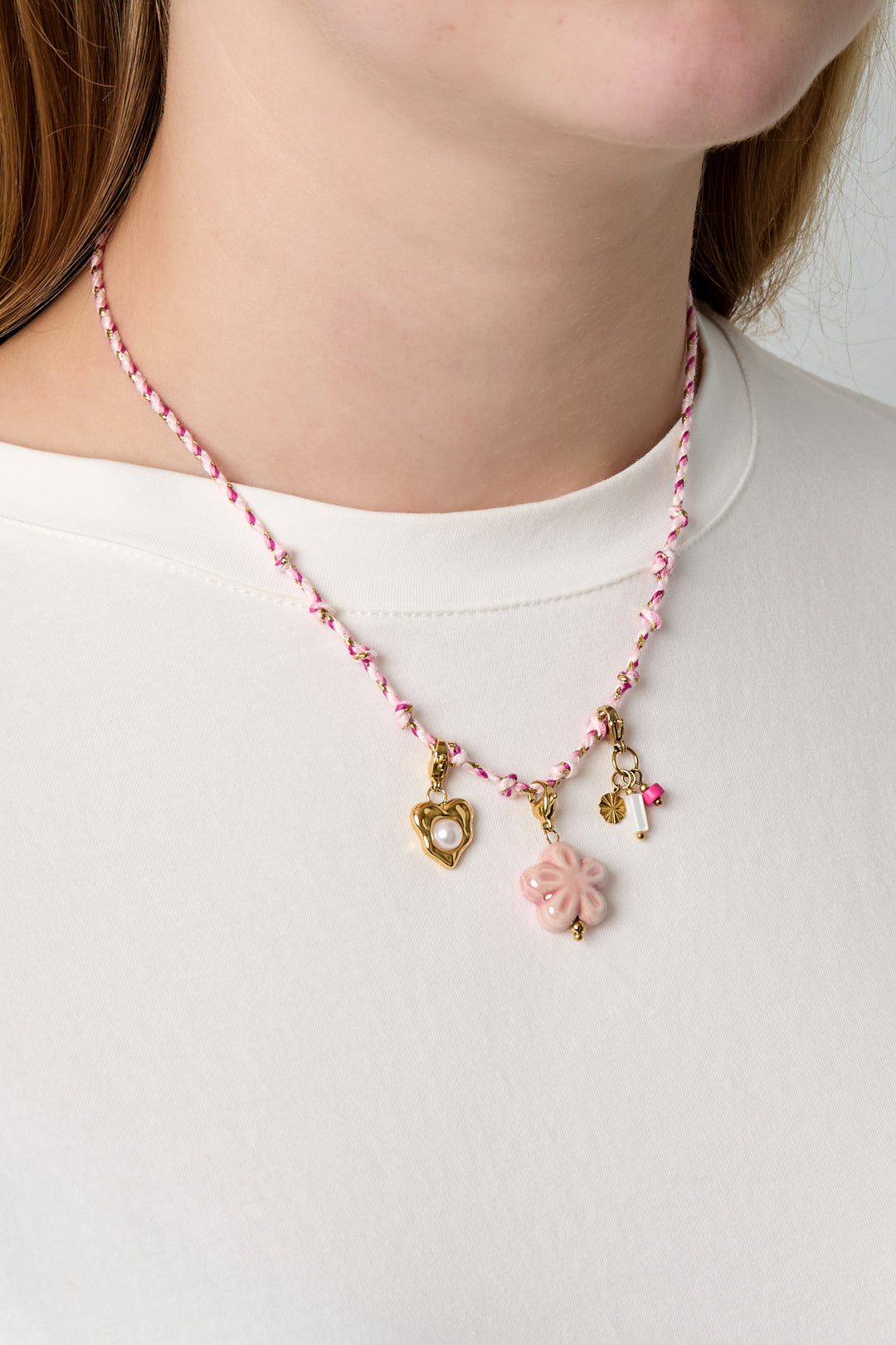 Close-up of pink knotted cotton necklace worn by female model over white shirt with three gold and pink charms