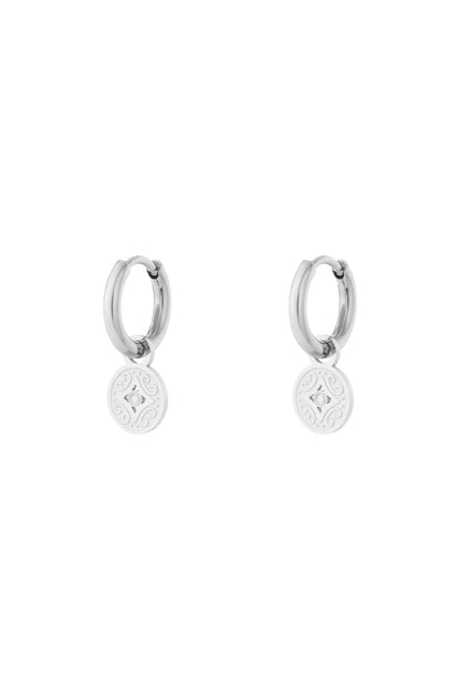 Silver-tone stainless steel hoop earrings with engraved round charm detail on white background