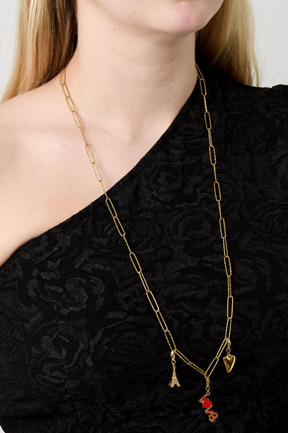 Gold elongated link chain necklace worn on a woman with black textured top, styled with small dangling charms