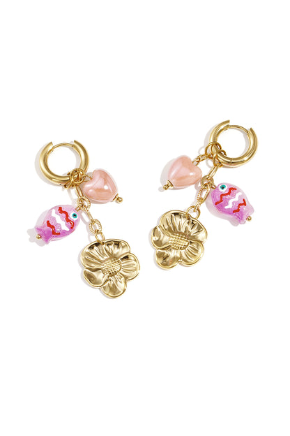 Pair of gold-tone drop earrings with pink fish, heart bead, and gold flower charms laid flat on white background