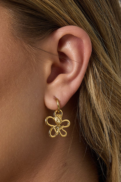 Detailed side view of a gold flower and rose drop earring on a woman's ear, highlighting lightweight design