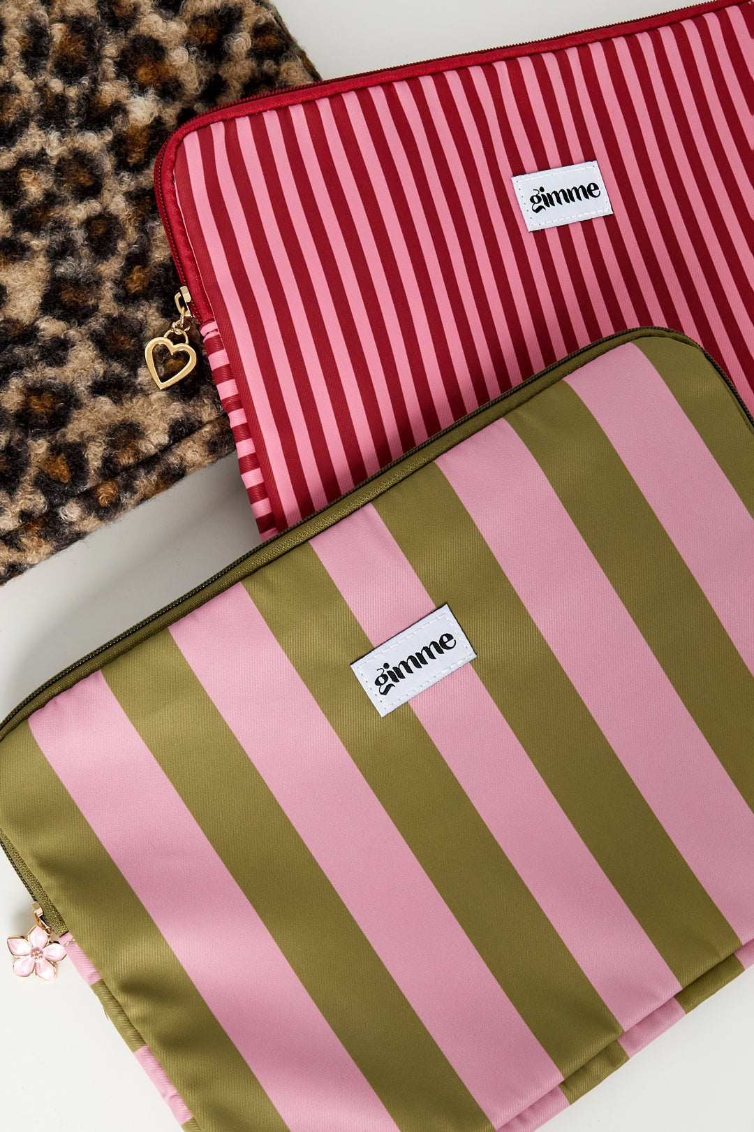 Two striped laptop sleeves in olive green pink and red pink with gold zipper charms on leopard print background