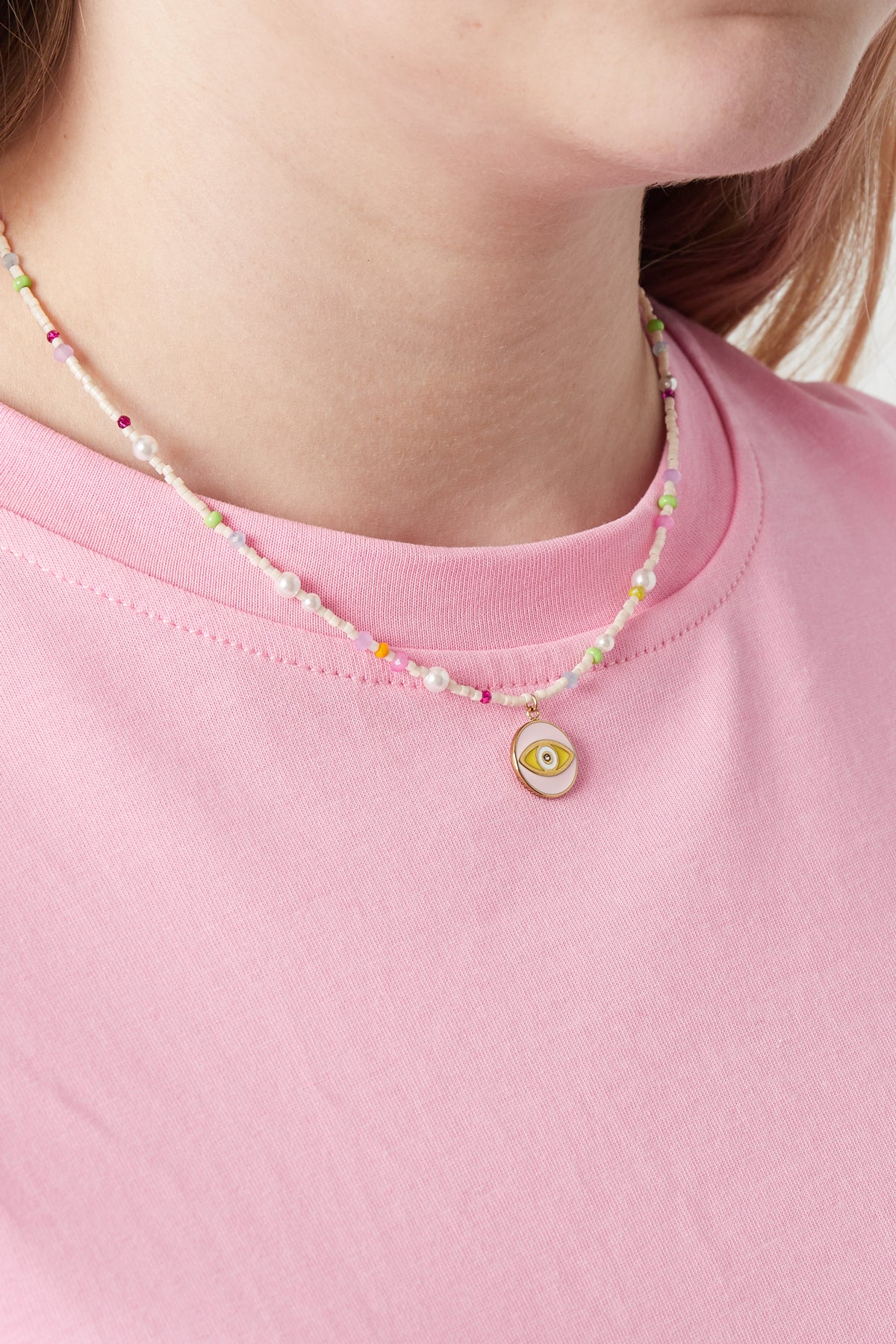 Model wearing pastel beaded necklace with yellow eye pendant and pink shirt