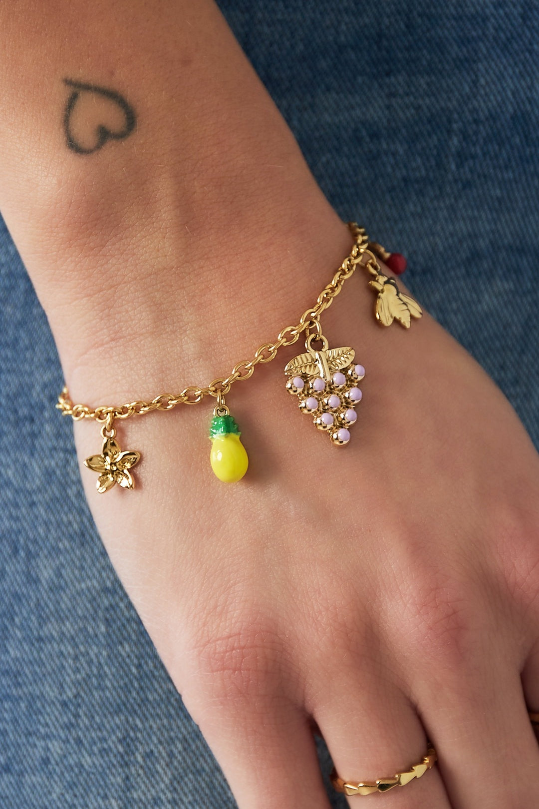 Close-up of wrist wearing the gold-plated fruity charm bracelet with flower, lemon, grape, bee, and cherry charms