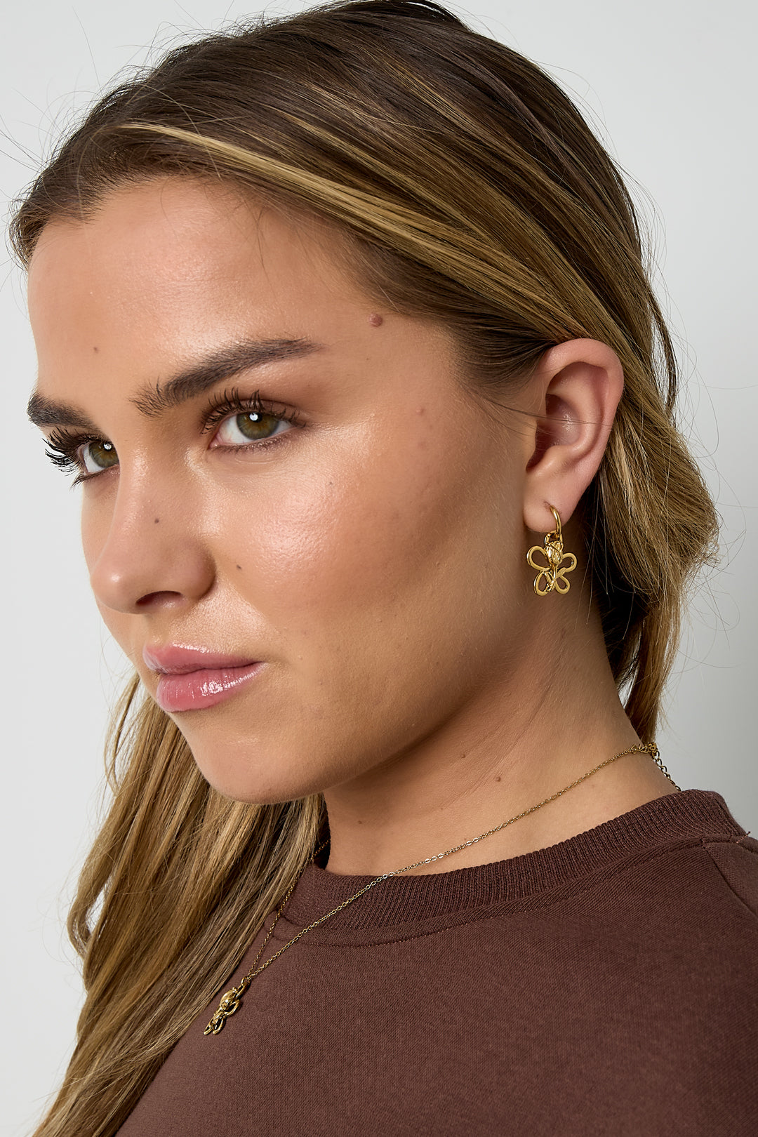 Close-up of a woman wearing gold flower and rose drop earrings, showing elegant fit and youthful style