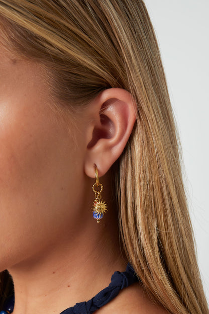 Model wearing gold tone hoop earring with sun charm and blue-orange bead, side profile view