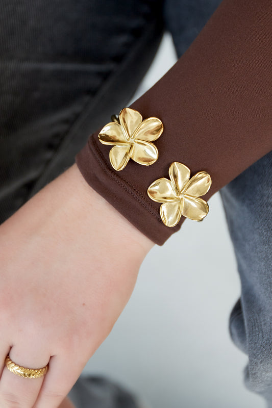 Close-up of gold floral cuff bracelet worn on wrist with brown long sleeve and gold braided ring
