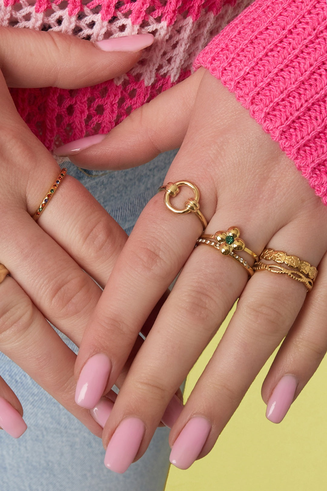 Close-up of woman's hand wearing the gold circle knot ring with layered other gold rings and pink nail polish