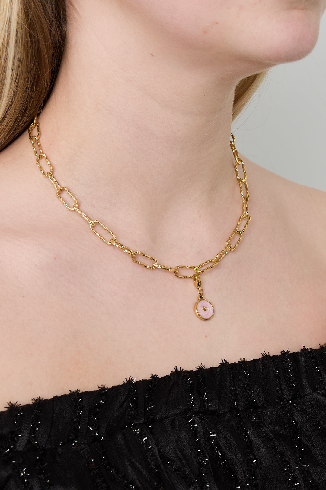 Gold textured link chain necklace with pink charm worn close-up on a woman in black top