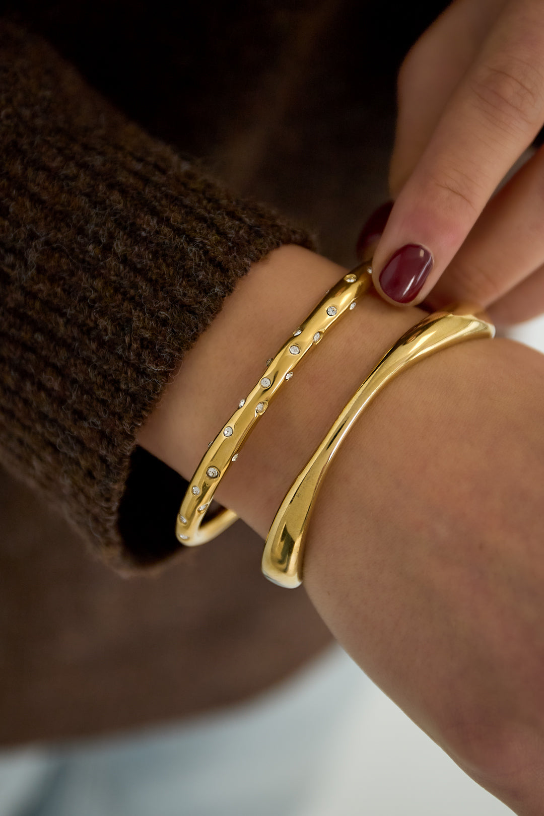 Close-up of two gold bracelets on woman’s wrist, one is an organic sculpted cuff and the other is studded with small crystals