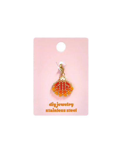 Red and orange beaded shell charm with a gold clasp on a pink display card.