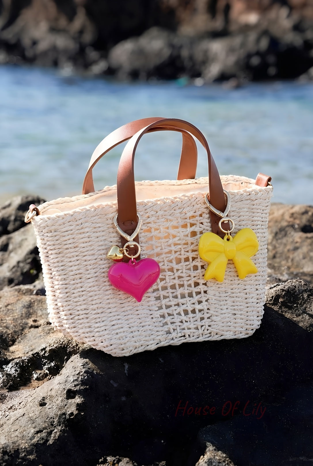 Beige woven handbag with brown leather handles decorated with pink heart and yellow bow acrylic charms by the sea