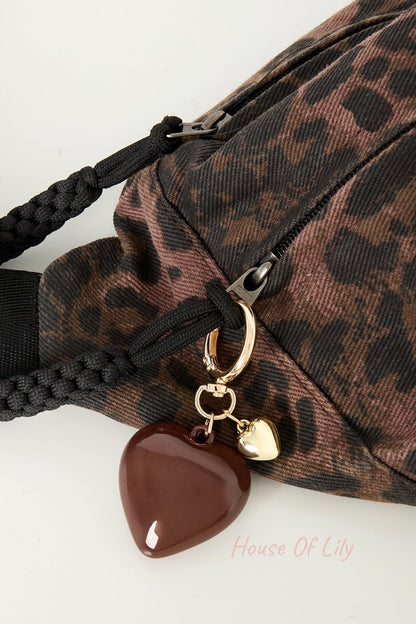 Close-up of brown heart charm clipped on dark patterned handbag zipper with braided handles