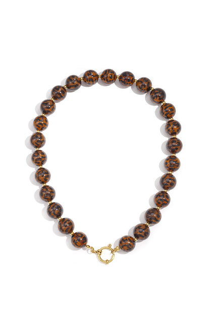 Close-up of medium-length acrylic beaded necklace with leopard print beads and gold toggle clasp on white background