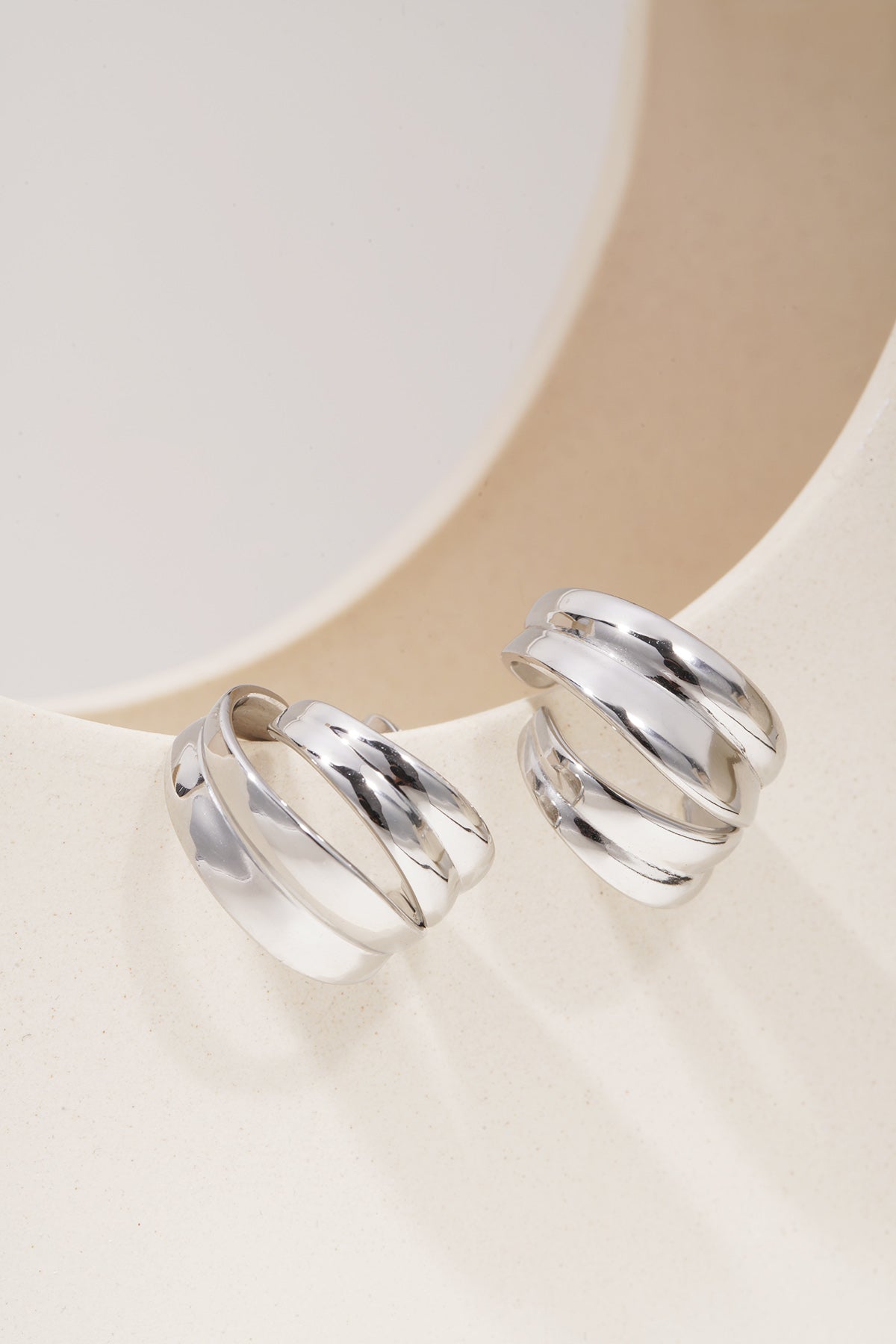 Sculpted Aura Loops: Pair of chunky, polished silver hoop earrings with a layered, multi-band design on a curved base.
